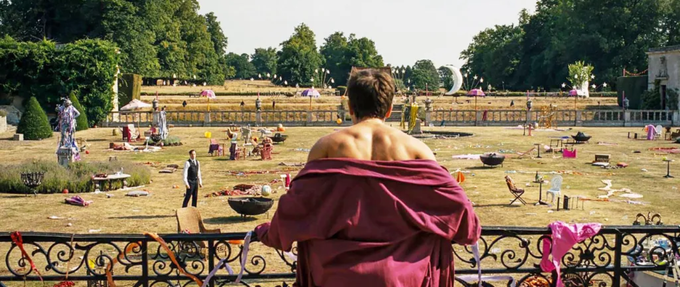 man in robe overlooking the disaster left on his lawn after a crazy party